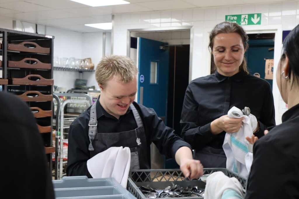 A young man with Down syndrome working in a kitchen with colleagues.