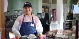 A woman standing at a counter wearing a black cap with Cafe Domenica logo on it and smiling