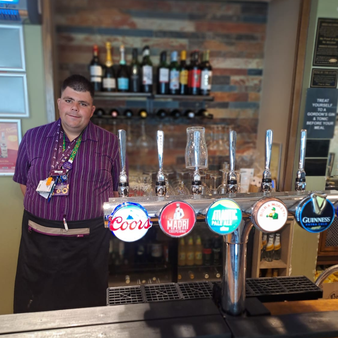A young man stands behind a bar after completing a supported internship.