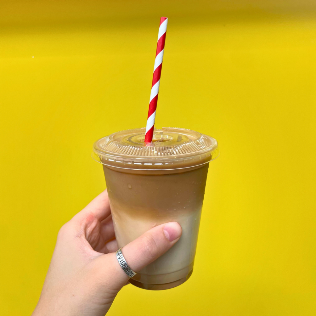 a person holds an iced coffee in their hand against a yellow background.