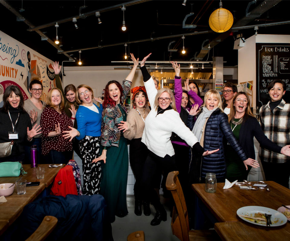 A group of women from our Co-Women partnership stand together laughing with their hands in the air.