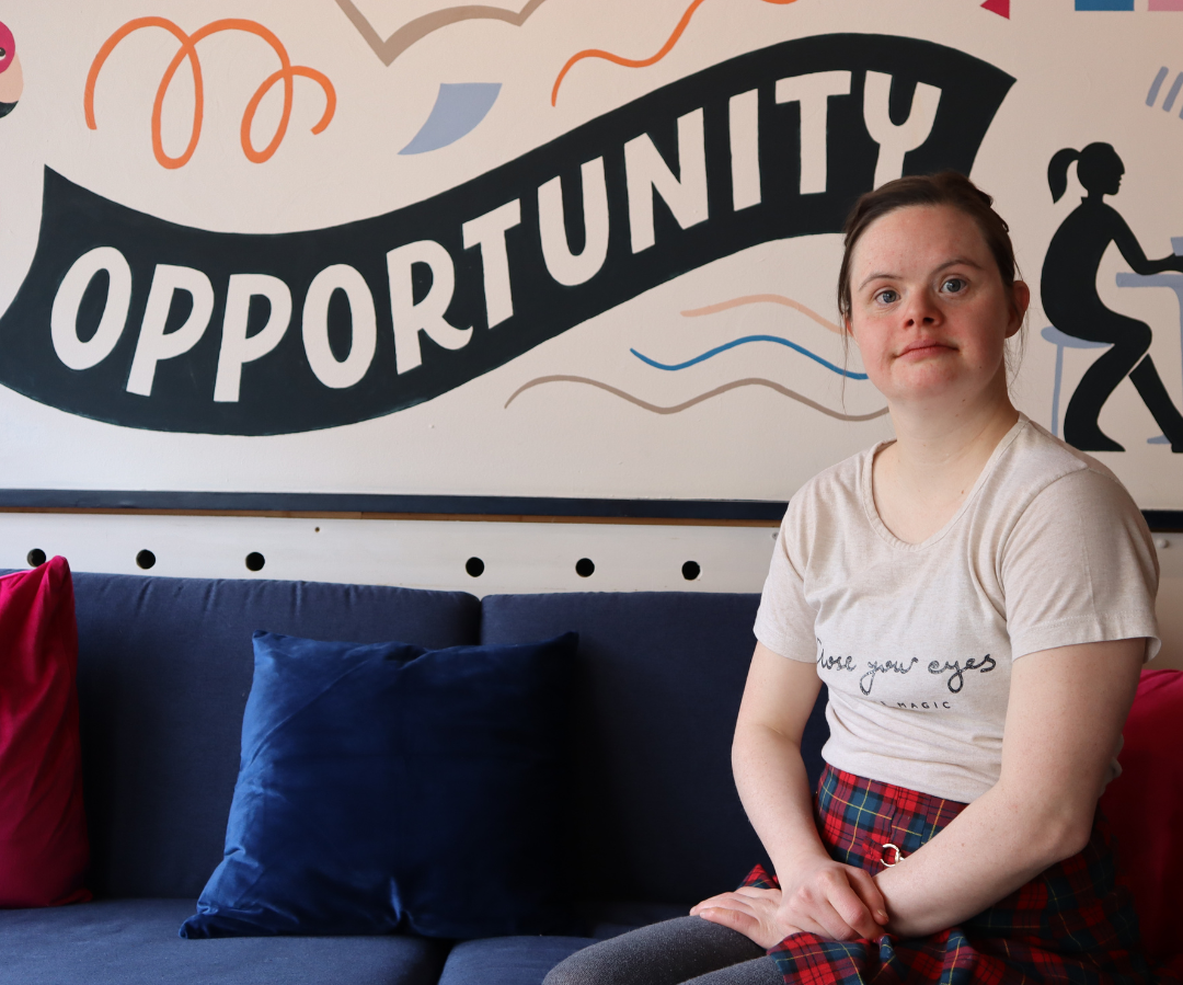 A photo of a young woman with Down Syndrome, called Florence, sat posing for the camera after talking about World Down Syndrome Day 2024.