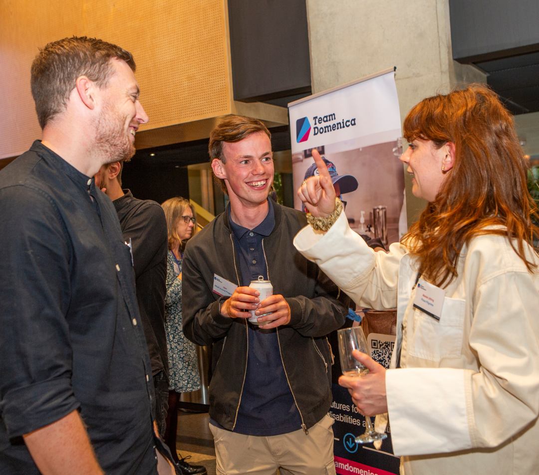 Three people stand together chatting and laughing. They are two employers and one candidate at Team Domenica's employer partner celebration - an event marking how local employers are working to improve inclusivity in the workplace.