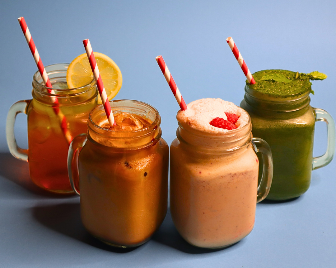 Four delicious summer drinks sit in a line – a peach iced tea, an iced coffee, a berry good smoothie and a green health shake.