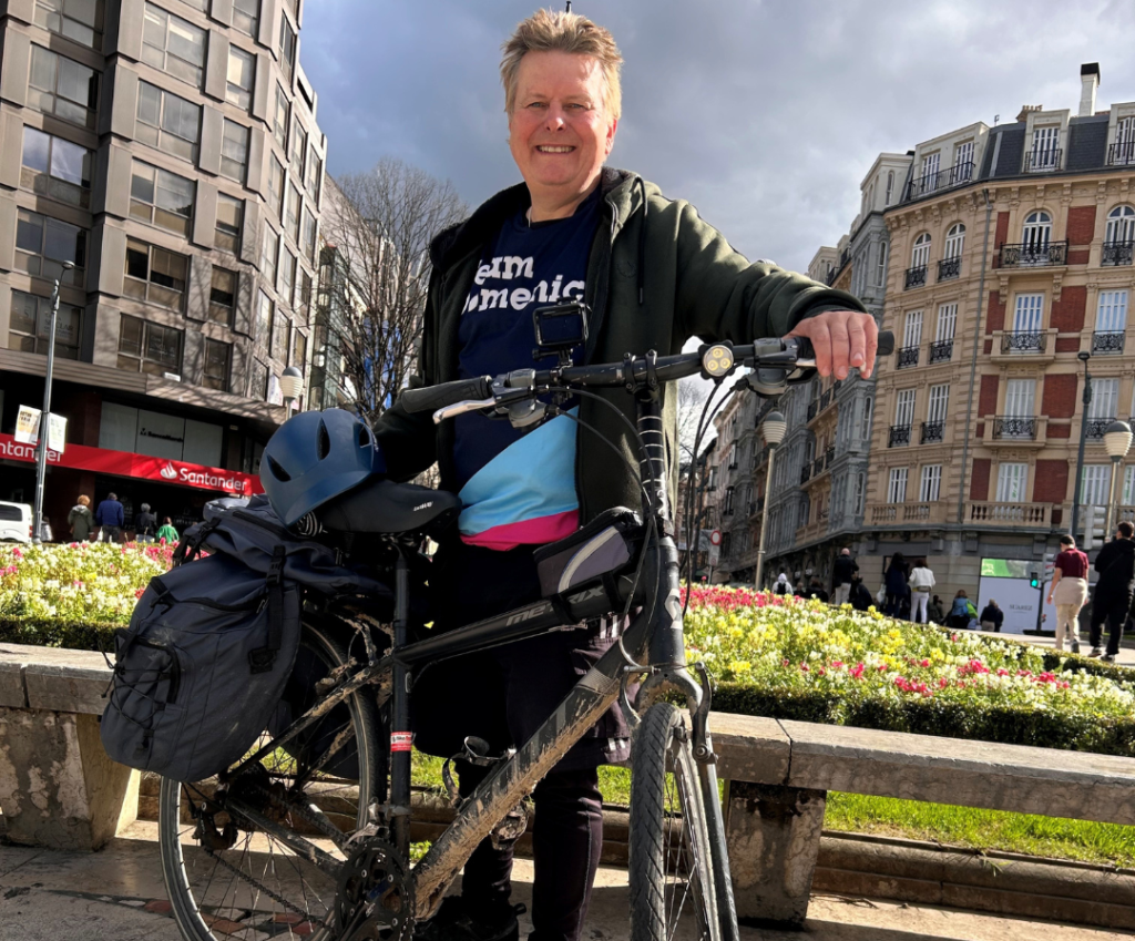 A man stands in Bilbao wearing a Team Domenica T-shirt. He is smiling from ear to ear after cycling the length of Spain in aid of Team Domenica.