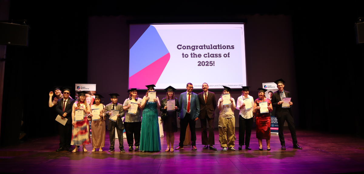 Graduates stand on a stage in front of a message that reads: "Congratulations to the class of 2025"