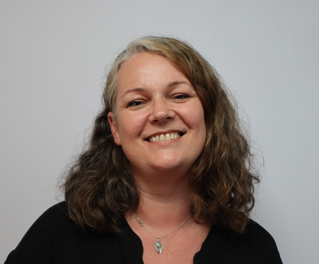 A headshot of Amanda Thomson. She is white and has brown / grey curly hair.