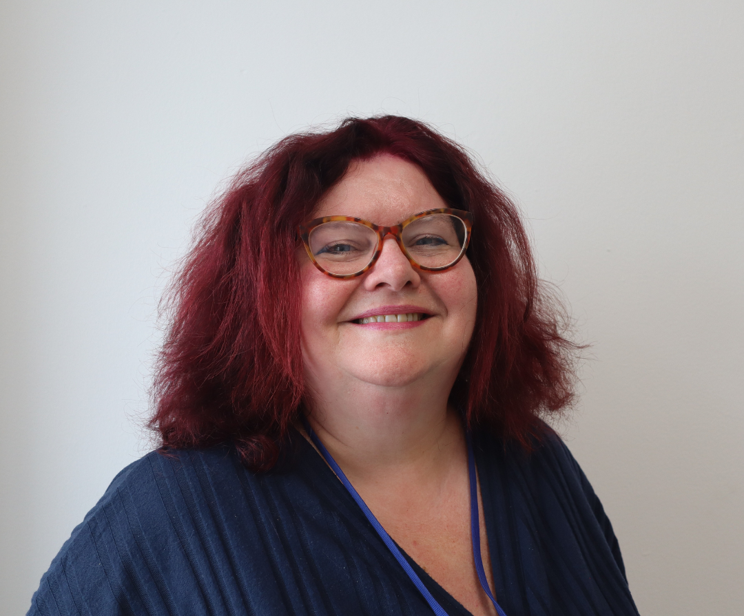 A headshot of Sara Fletcher. She is white, has red hair and glasses.